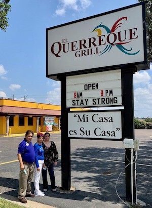Restaurant owners stand in front of El Querreque Grill sign.