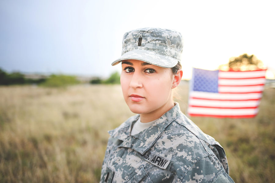 A woman in Army fatigues stands with an American flag in the background