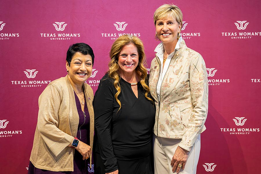 business college dean Rama Yelkur, Merrilee Kick and Chancellor Carine Feyten in front of a maroon TWU backdrop