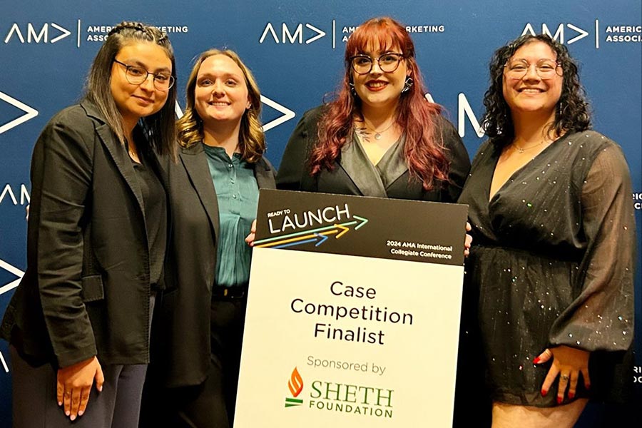 Four young women dressed in suits stand in front of a AMA blue backdrop