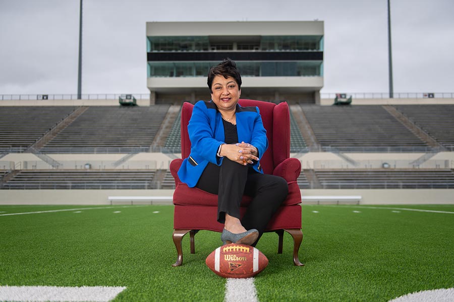 MAK College Dean Yelkur sits on a chair with her foot on a football on the 50-yard line