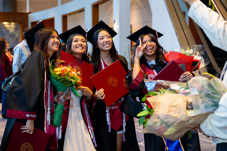 Four TWU Houston graduates pose in academic regalia for a photo.