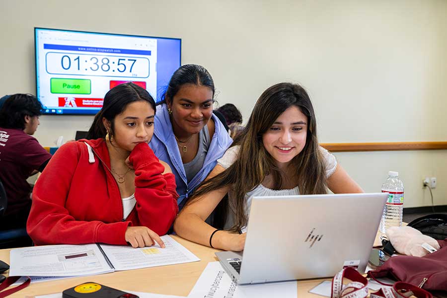 Computer Science students collaborate in a classroom setting around a laptop.