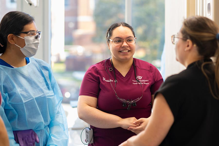 three students in TWU scrubs stand and converse in the dental hygiene clinic