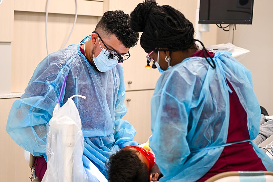 Two dental hygiene students work on a patient in a dental chair 