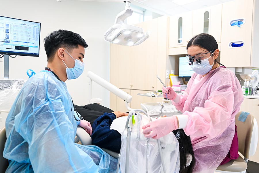 Three women wearing scrubs looking at computer screen with health clinic machinery in background