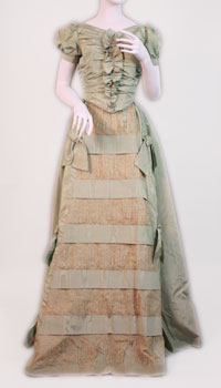 The dress is made of turquoise moir&eacute; taffeta trimmed with bows and has lace inserts on front panel. 