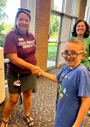 TWU staff member in maroon shirt shakes hand with camper in blue shirt 