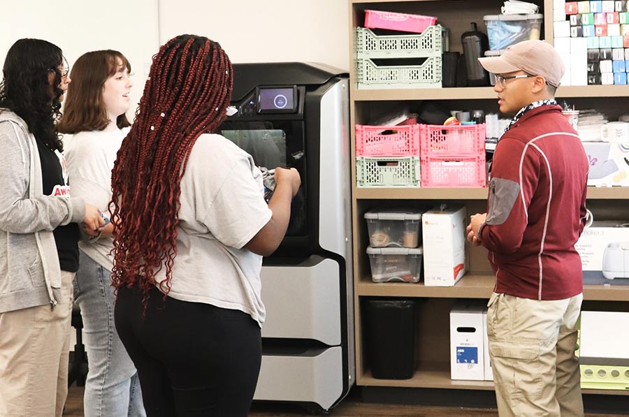 Inside Makerspace, staff member shows a group of students the plethora of supplies lining the walls.