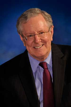 A headshot of Steve Forbes in a suit with a blue background.
