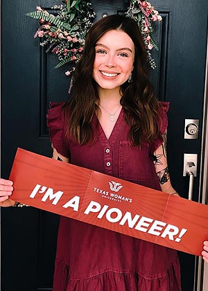 student holding an I'm a Pioneer sign in front of a door