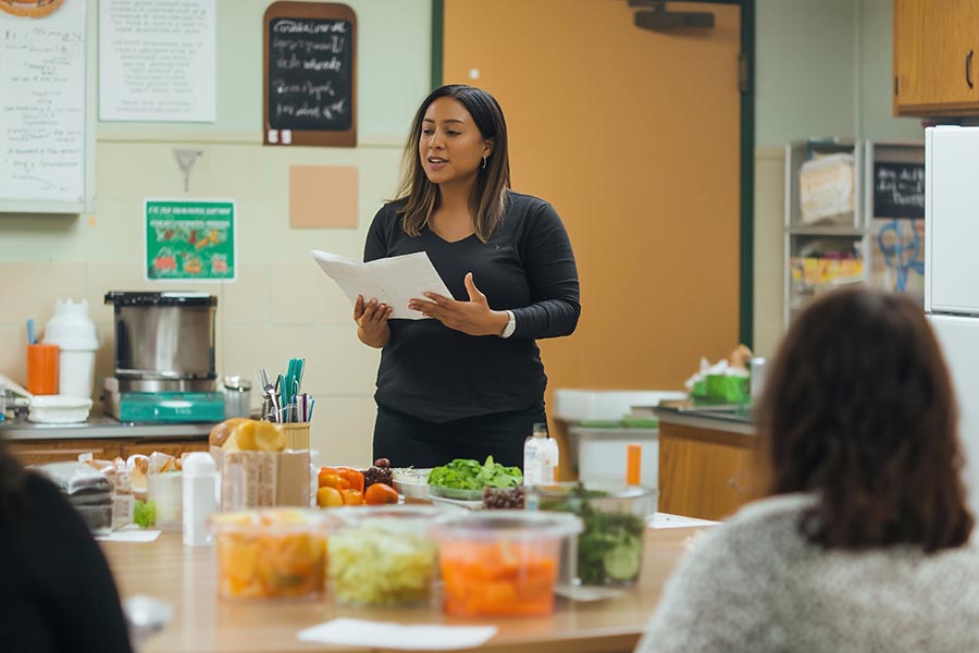 a nutrition student talks to three people in front of table with food
