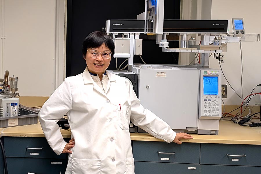 a professor in a lab coat stands next to a counter with a machine