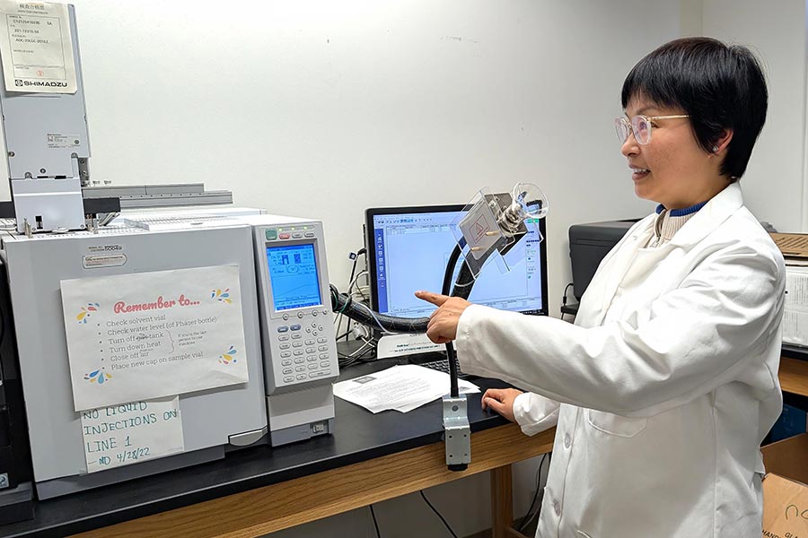 a professor in a lab coat points at a machine in a lab