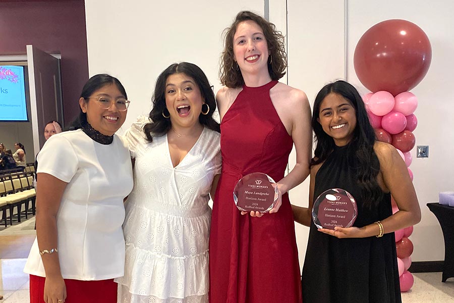 four female students stand together with two on the right holding plaques at awards ceremony