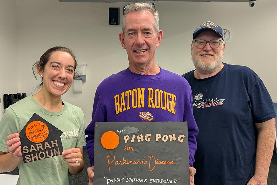 TWU student holds a sign and stands next to a man in a purple shirt with a sign and a man in a blue shirt and hat