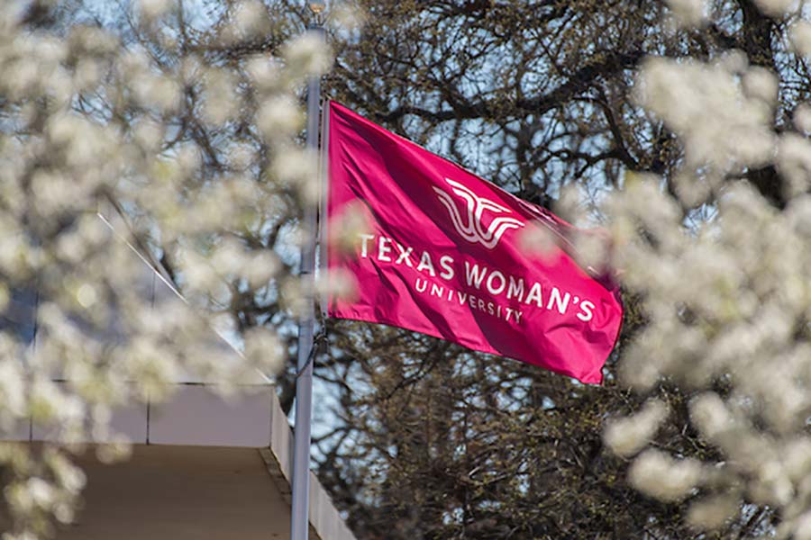 maroon TWU flag waves in the wind among white flowers